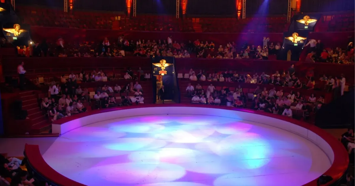 A large tango theatre seen from the upper tier before the show, a lit round stage below and the audience filling the red tiers