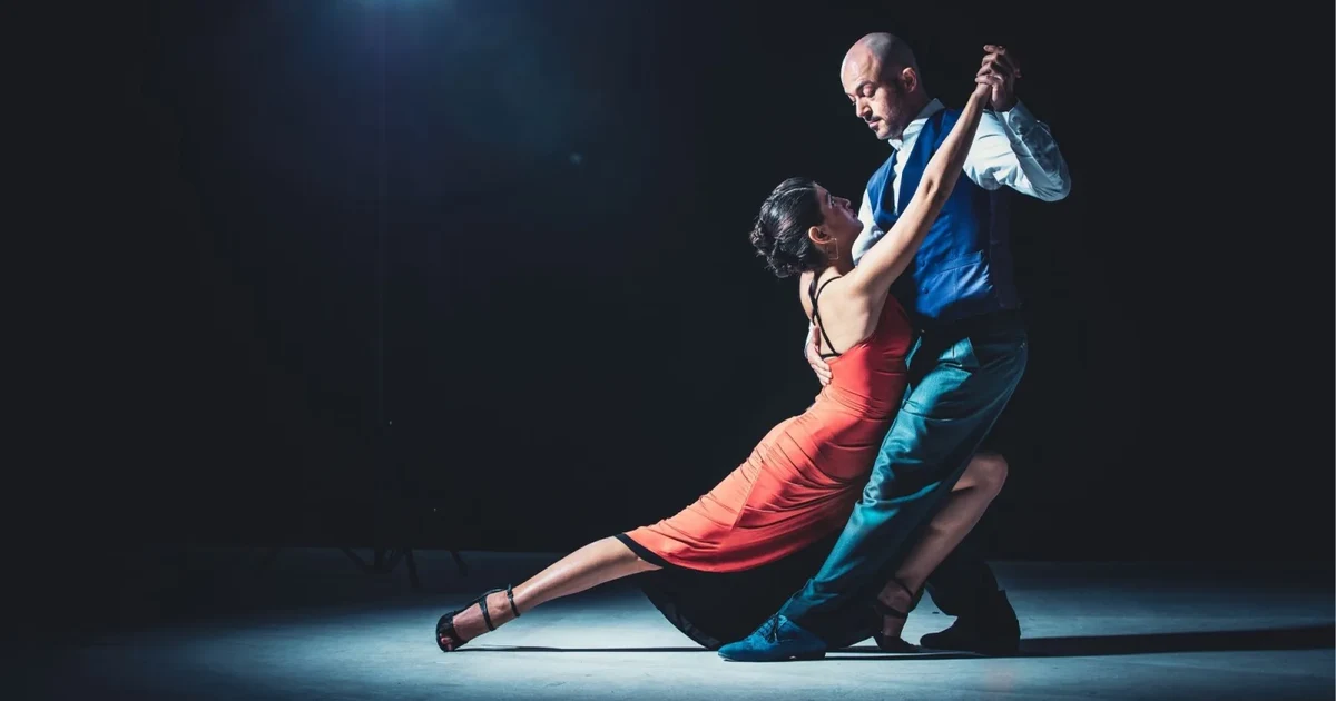 A tango couple mid-dip on a dark stage, representing the evening a hotel transfer package delivers you to