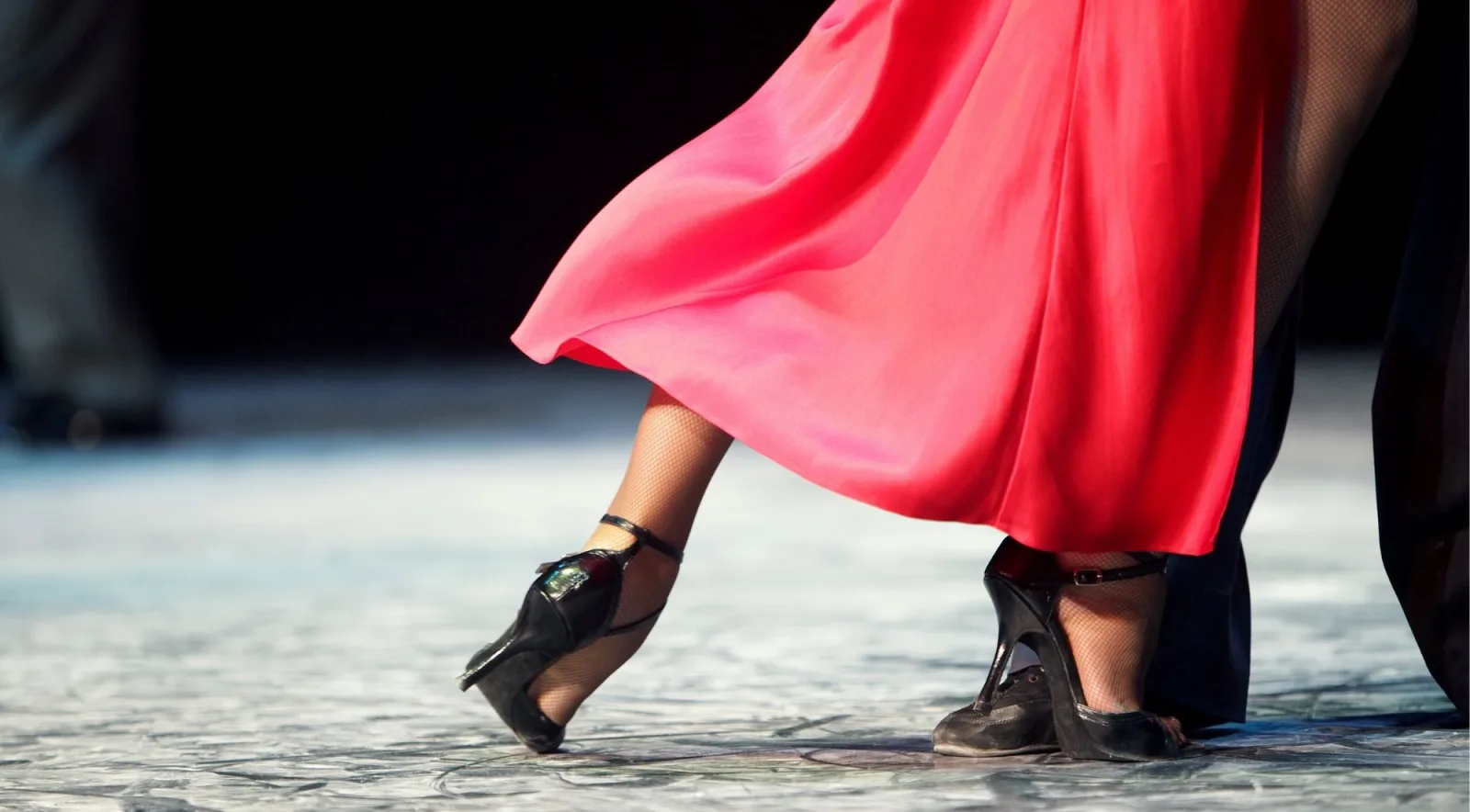 Close crop of dancers' feet on a worn floor, a red skirt sweeping past a heeled shoe