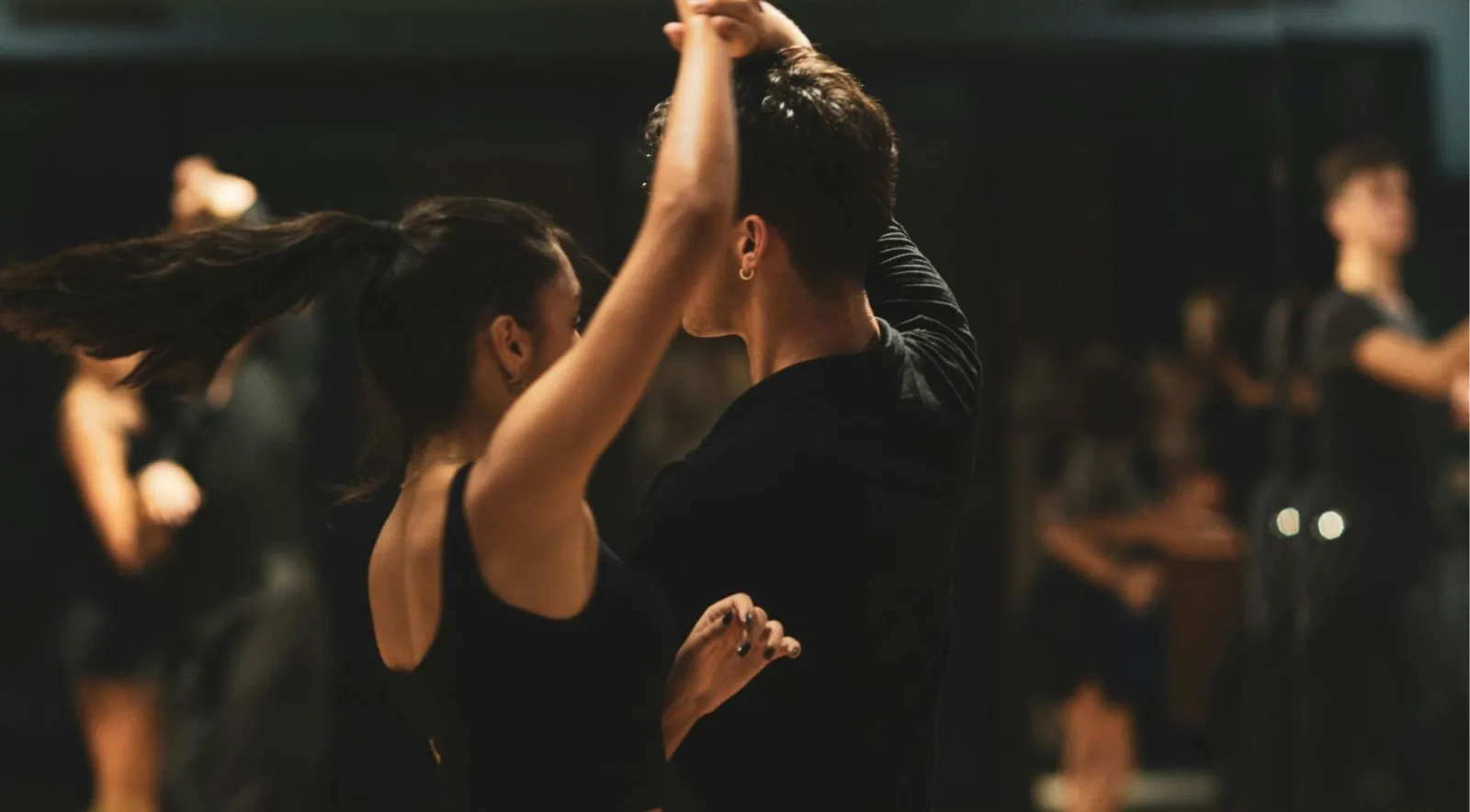 Several couples dancing together on a dimly lit milonga floor, hair caught in motion