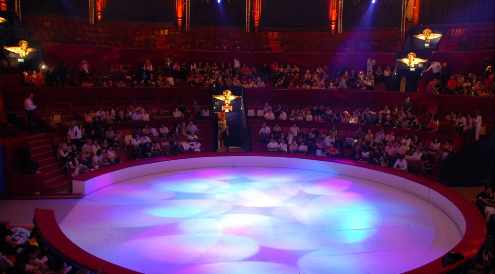 A large tango theatre seen from the upper tier, circular lit stage below and gilt boxes around a full house