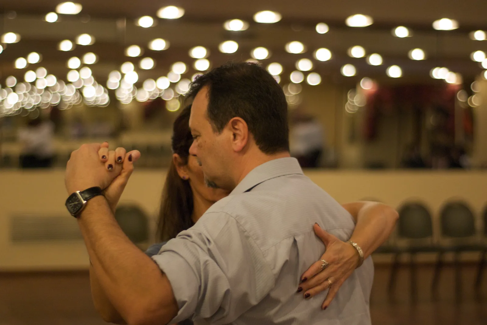 Two dancers holding the tango embrace in a bright, high-ceilinged practice hall