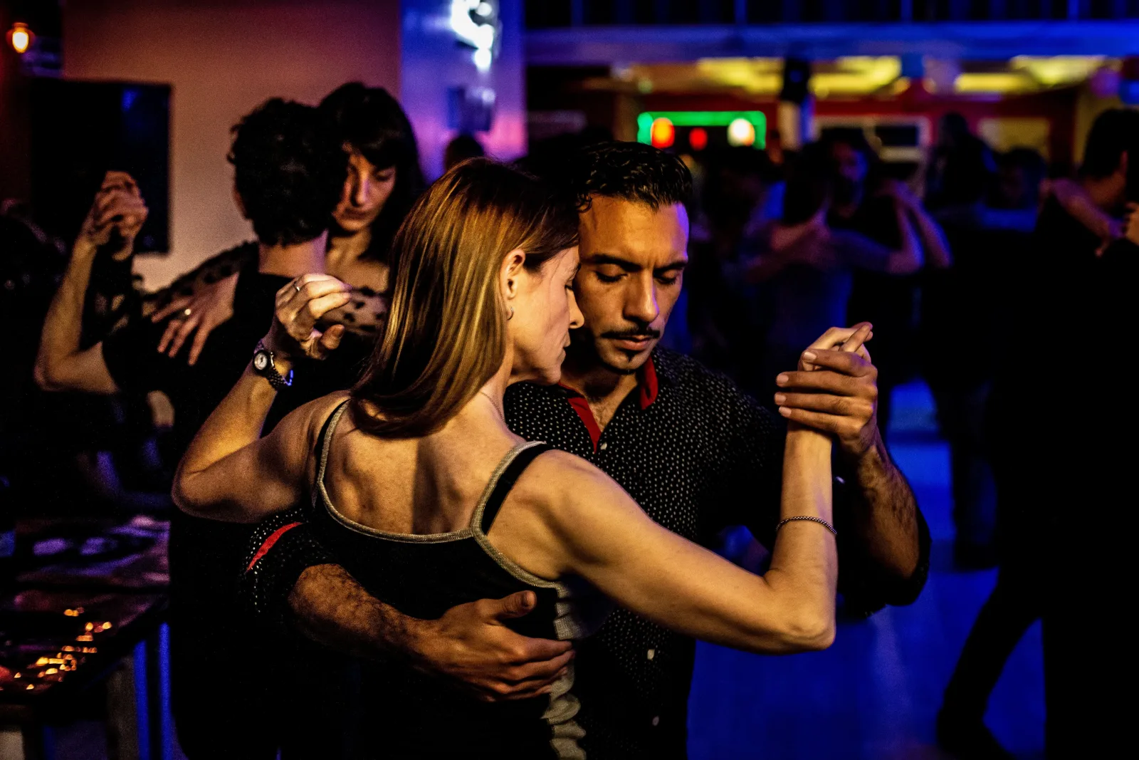 Several couples dancing tango close together in a dimly lit milonga