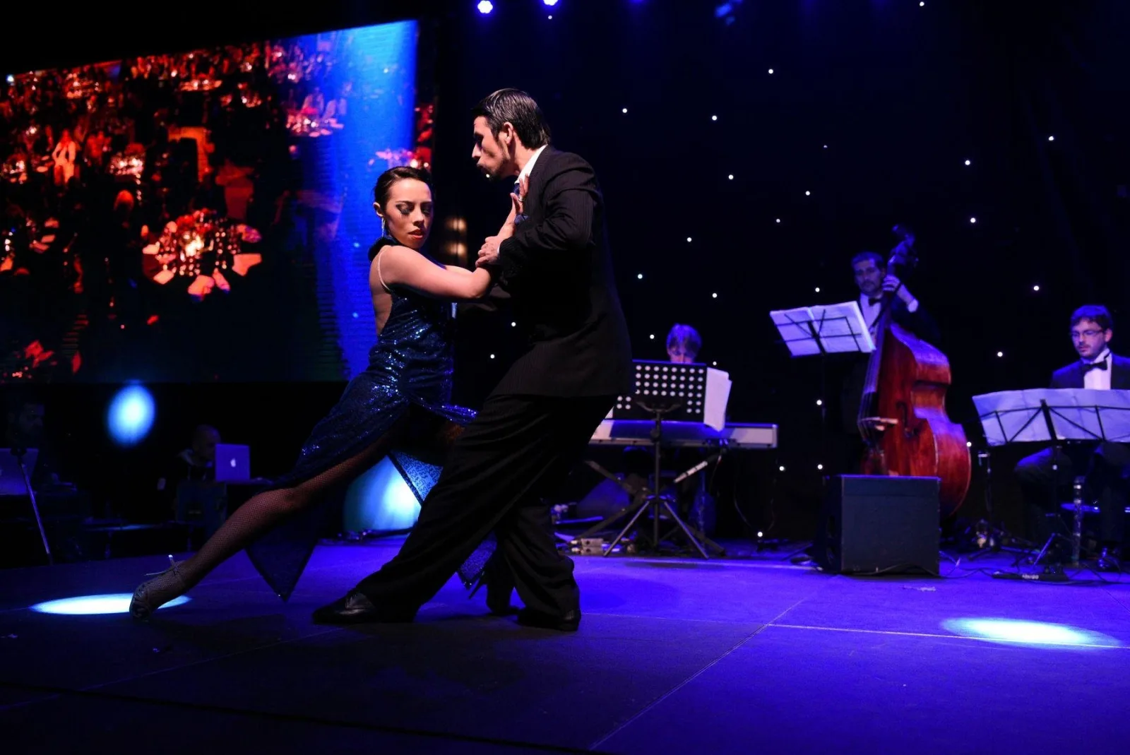 A tango couple dancing under blue light beside the El Viejo Almacén live orchestra