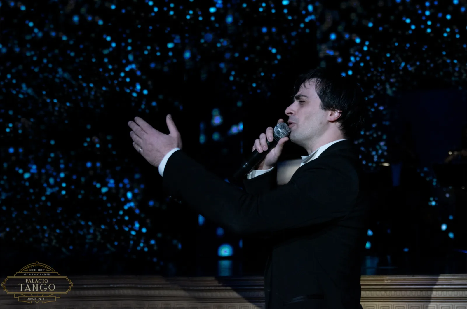 A male tango vocalist singing under blue stage lights at Piazzolla Tango