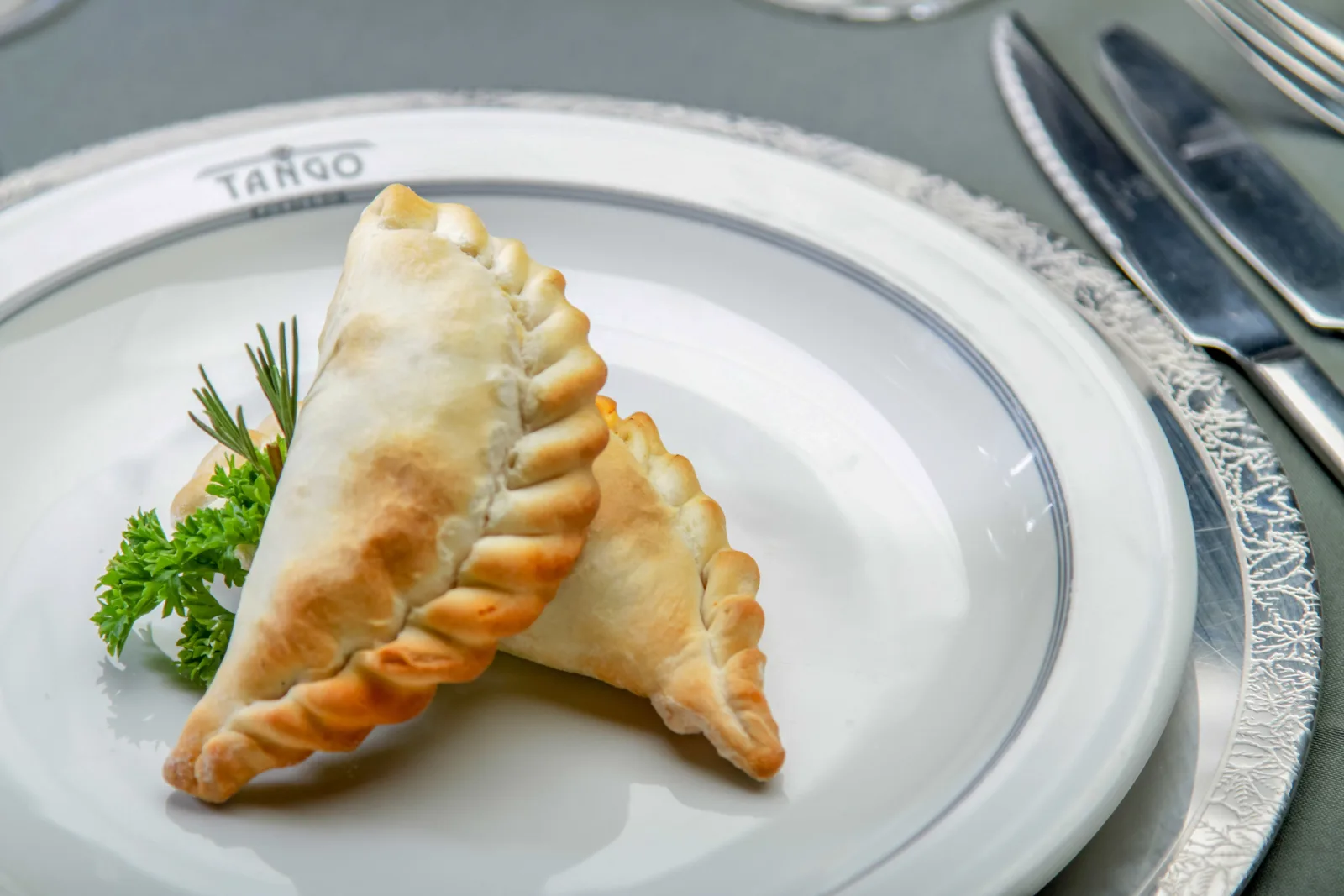 Two Argentine empanadas on a Tango Porteño plate with parsley garnish