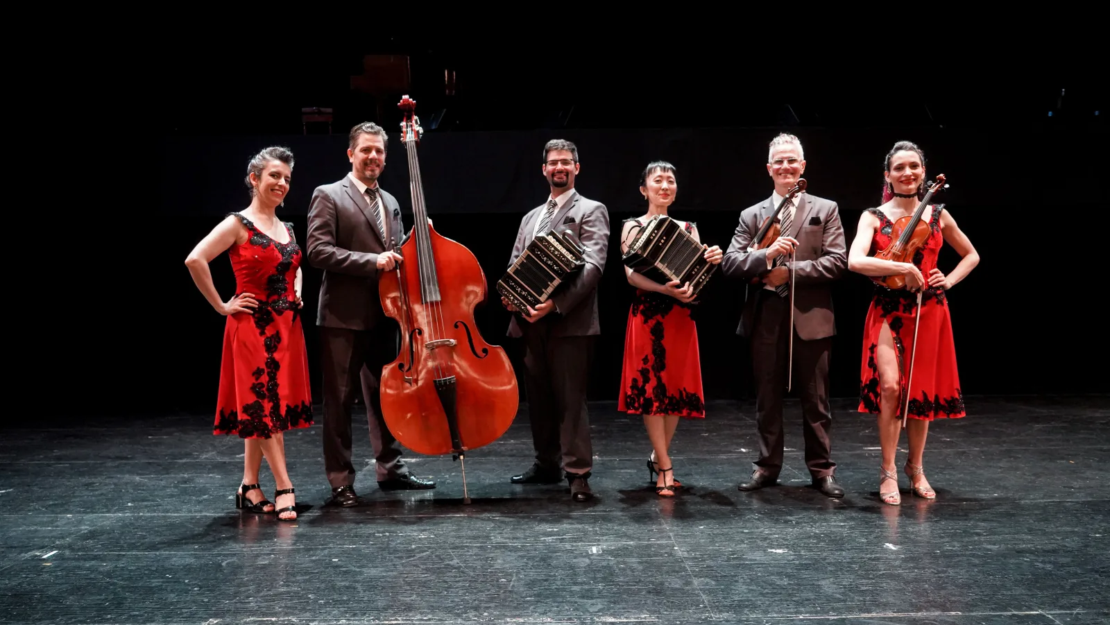 The Tango Porteño orchestra and dancers posed together on stage with a double bass