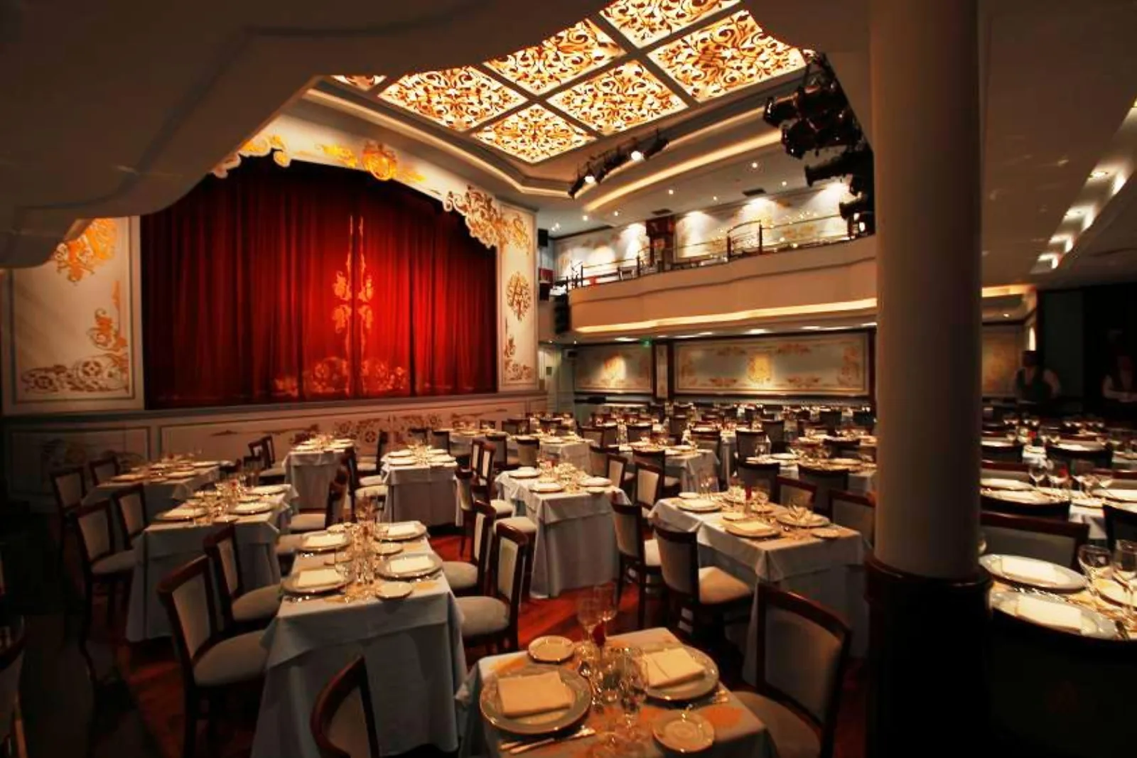 The Café de los Angelitos dining room, tables laid in front of the red stage curtain