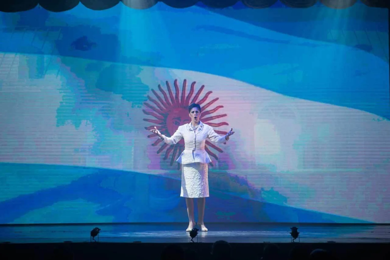 A solo performer on the Madero Tango stage in front of a large projected Argentine flag