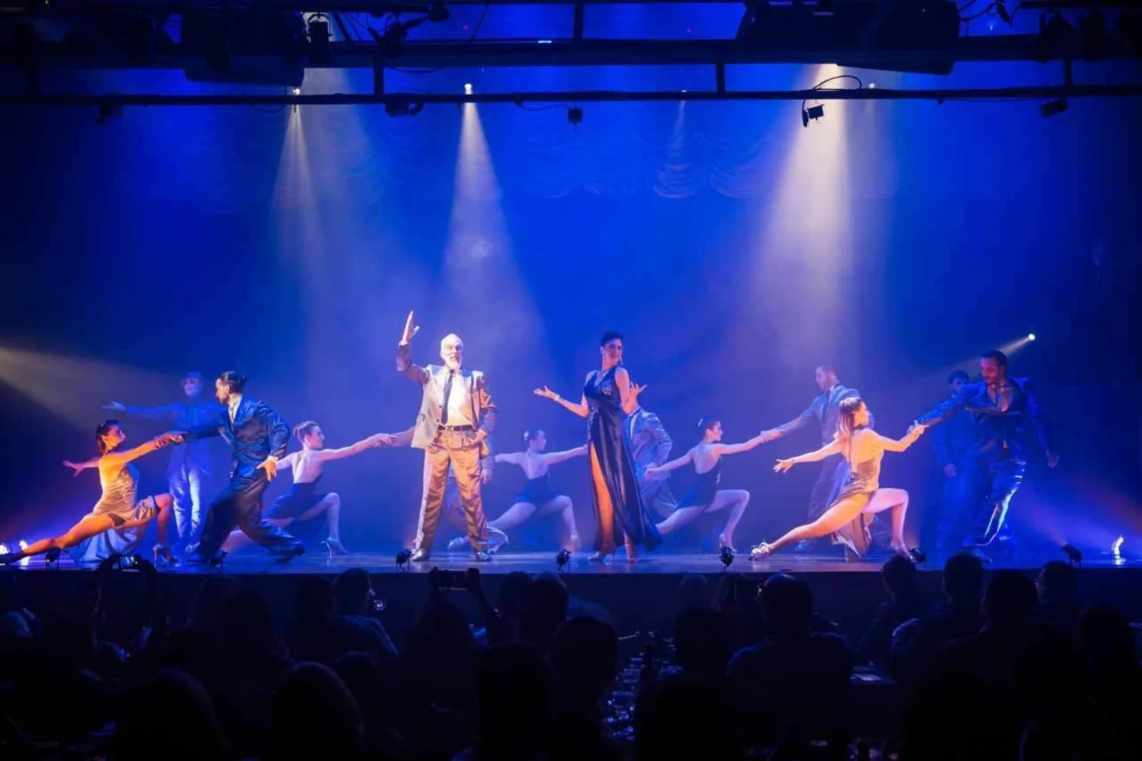 The Madero Tango company dancing in formation under blue and white stage lighting
